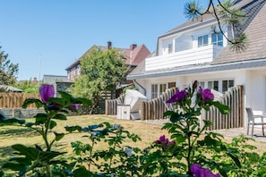Een woonhuis met een overdekt terras, een omheinde achtertuin en een boom.
