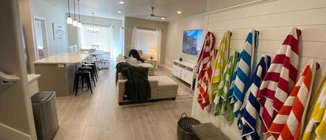 A modern living room with a sofa, a dining area, a TV, and a wall with colorful towels.
