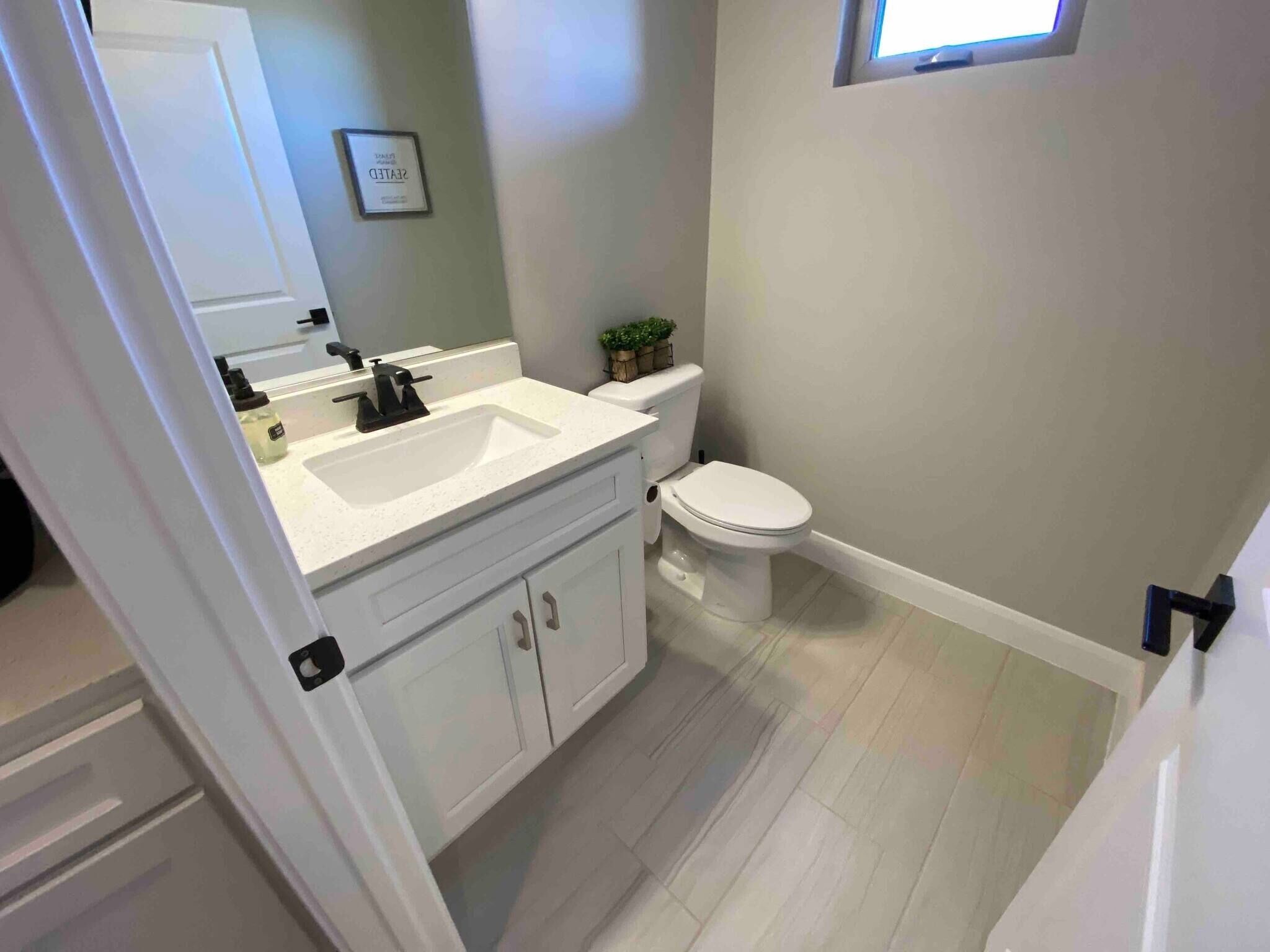 A bathroom with a white sink, vanity, and toilet. There is a small window above the toilet.