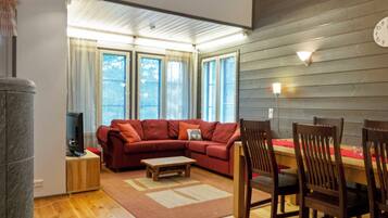 A living room with a sectional sofa, a coffee table, wooden chairs, a TV, and a dining table with chairs.