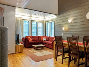 A living room with a sectional sofa, a coffee table, wooden chairs, a TV, and a dining table with chairs.