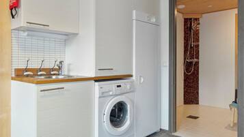 A compact laundry area with a washing machine, a sink, and a shower.