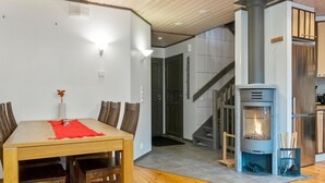 Een moderne keuken met een houtkachel, een eethoek met een houten tafel en stoelen, en een trap naar een ander niveau.