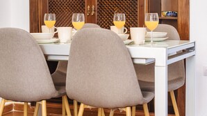 A dining area with a wooden cabinet, a white table, and four grey chairs with wooden legs. - Homey Seville. Bright Apartment in Santa Cruz (Sleeps 6; Parking Optional) (Sevilla)