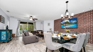 A modern living room with a dining area, featuring a brick wall, a large TV, and a ceiling fan. - 

PerfectVacationHome5/4 Sleep12close to DisneyWorld, great forfamily gathering  (Kissimmee)