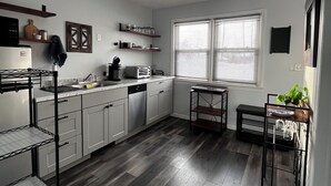 Une cuisine moderne avec des meubles blancs, un plancher en bois et une fenêtre équipée de stores.