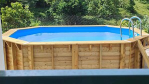 A wooden above-ground swimming pool with metal ladders, surrounded by a chain-link fence and lush greenery. - Sunbeam Bottom of villa T3 beach 2km away  (Sainte-Anne)