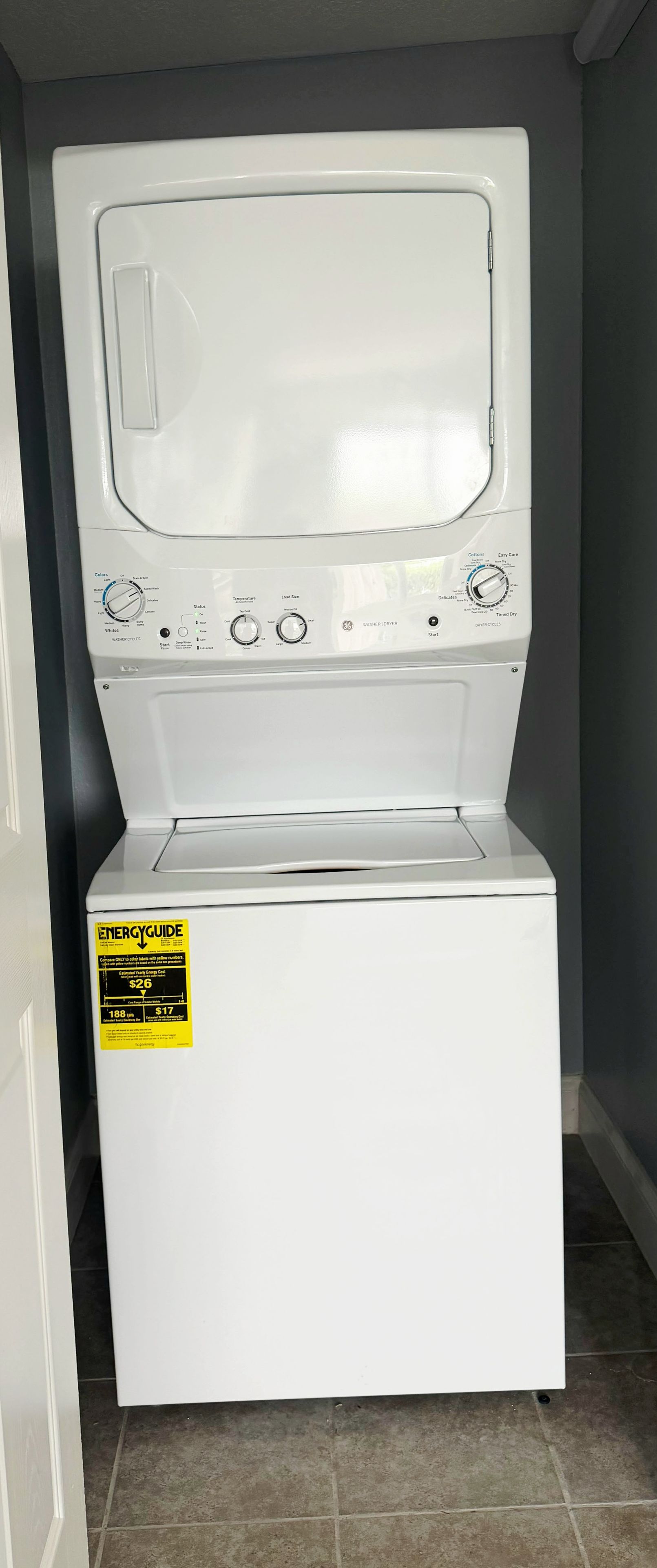 A front view of a white front-loading washing machine with a control panel and a sticker on the front.