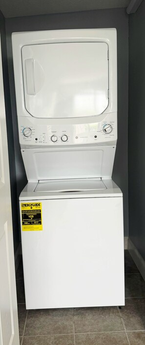A front view of a white front-loading washing machine with a control panel and a sticker on the front.