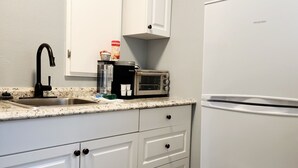 A kitchen with white cabinets, a black faucet, a toaster oven, and a refrigerator. - Lovely One Bedroom Home (Lakeland)