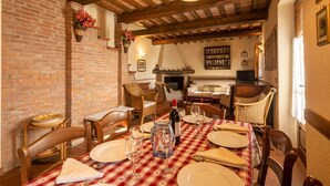 A dining area with a brick wall, wooden ceiling beams, and a table set for four with wine glasses and plates.
