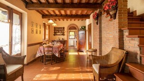 A dining area with a table set for two, wicker chairs, a brick wall, and a wooden ceiling.