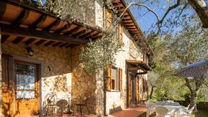A stone house with a wooden porch, outdoor seating, and a tree.