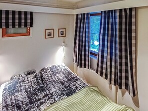 Une chambre à coucher avec un lit, une fenêtre avec des rideaux et deux tableaux encadrés accrochés au mur.