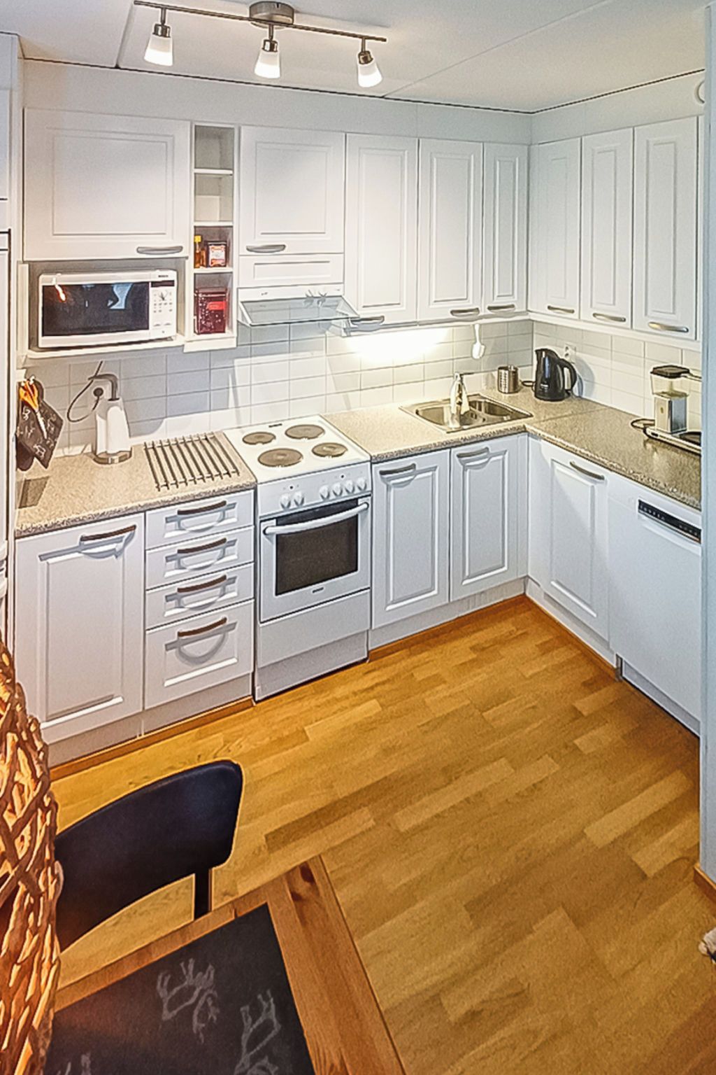 Une cuisine de taille réduite avec des meubles blancs, un four à micro-ondes, une cuisinière et un évier.