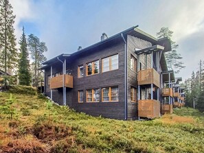 Une maison moderne à deux étages, dotée d’une façade sombre, de nombreuses fenêtres et de balcons en bois.