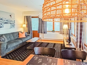 En moderne stue med sofa, to stole, sofabord og en dekorativ pendel.