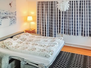 A bedroom with a bed, a nightstand, a lamp, a window with curtains, and a radiator.