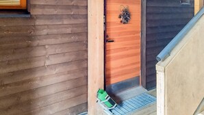 Una porta di legno con un piccolo portico, un gradino in metallo e un oggetto verde a terra.