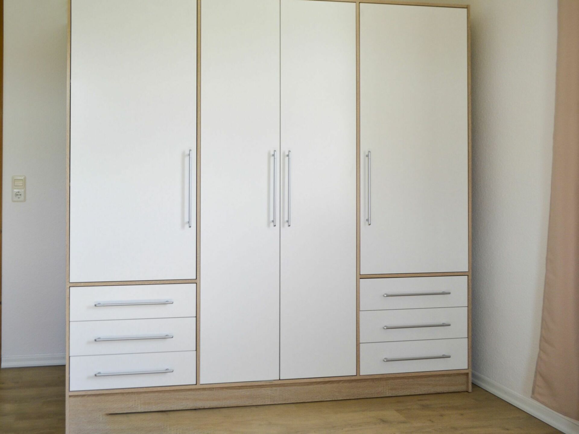 Un armario grande y blanco con varios cajones y puertas, que presenta una base de madera y tiradores de metal.