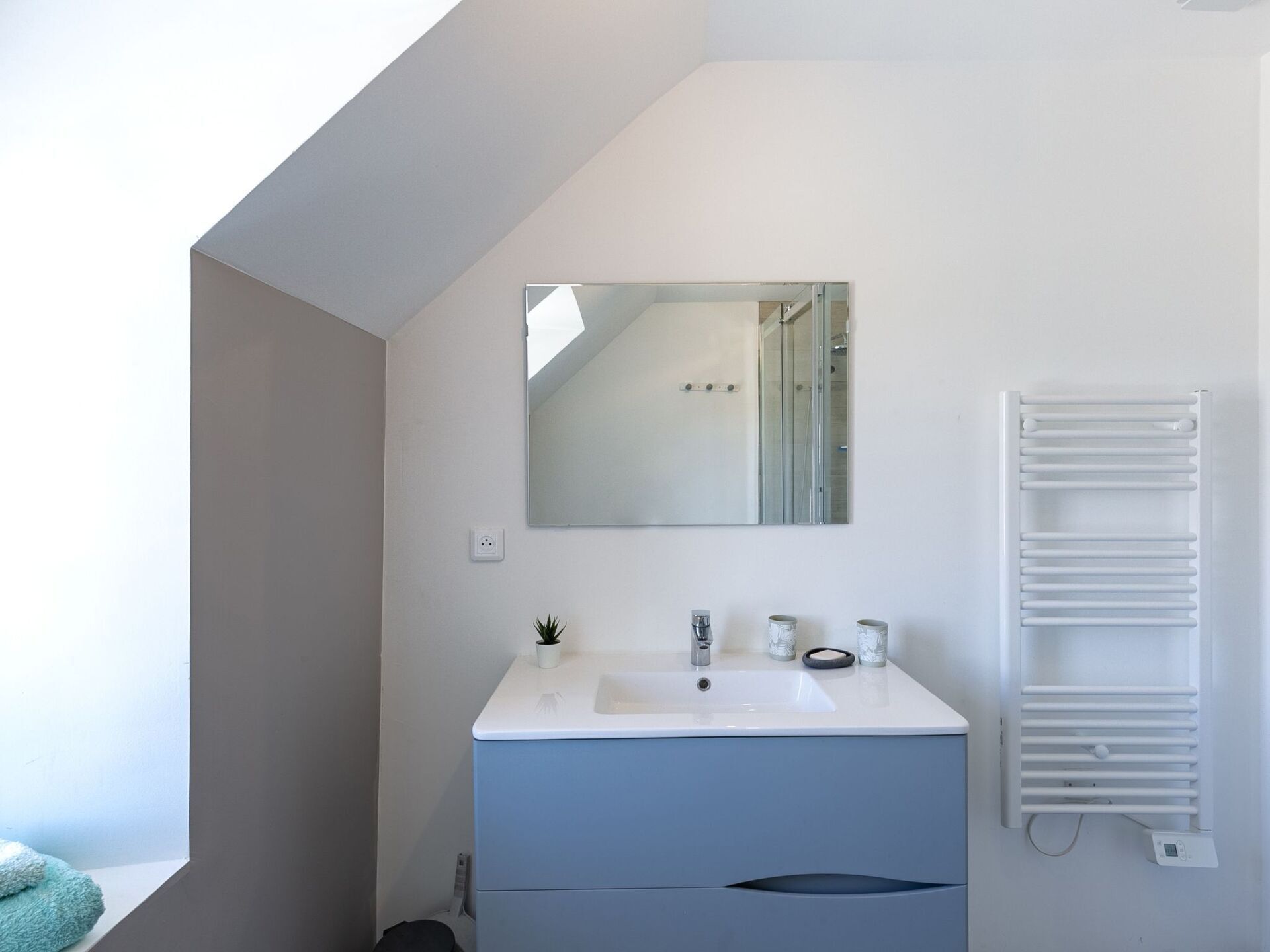 Un baño moderno con un lavabo blanco, un espejo y un perchero para toallas.