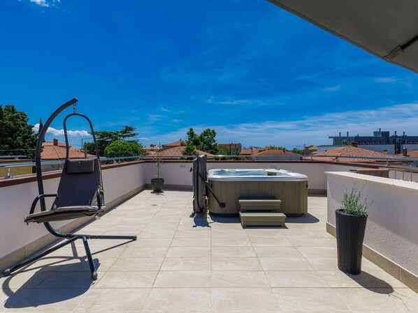 A rooftop terrace with a hot tub, a chair, and a potted plant.