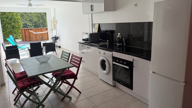 Une cuisine compacte équipée d’un lave-linge, d’un four et d’un coin repas avec une table et des chaises.