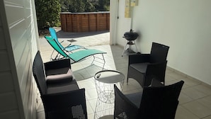 Une terrasse avec des meubles d’extérieur, un barbecue et une vue sur une plateforme en bois et des arbres.