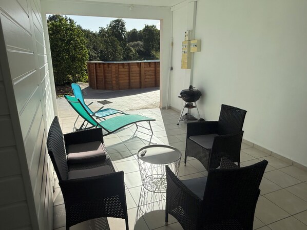 Une terrasse avec des meubles d’extérieur, un barbecue et une vue sur une plateforme en bois et des arbres.