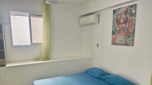 Une chambre à coucher avec un lit, une fenêtre avec des rideaux, un appareil de climatisation et un tableau accroché au mur.