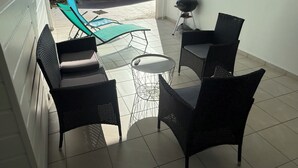 Une terrasse dotée de meubles en osier, d’un barbecue et offrant une vue sur le jardin.