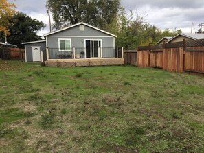 A single-story house with a front deck, a fenced backyard, and a wooden fence in the background.