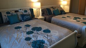 Zwei Betten mit je einem Einzelbett, blumigem Bettbezug, Nachttischlampen und eine Holztür im Hintergrund.
