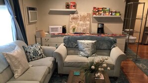 Ein Wohnzimmer mit zwei Sofas, einem Couchtisch mit Kiefernzapfen, einer Mikrowelle und einem Regal mit Snacks.