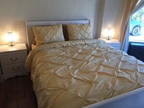 A neatly made bed with a quilted headboard, two bedside tables with lamps, and a window with a view of the outside.