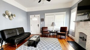 A living room with a black leather sofa, a coffee table, two chairs, a fireplace, and a ceiling fan.