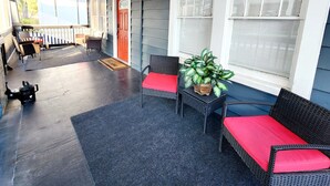 A covered porch with wicker furniture and a potted plant.