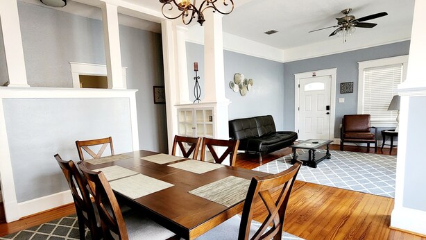 A dining area with a wooden table and chairs, a chandelier, and a ceiling fan.