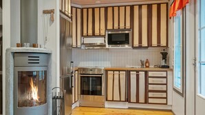 A modern kitchen with a wood-burning stove, stainless steel appliances, and a large window with orange curtains. - Pulkka 2 by Interhome (Salla)