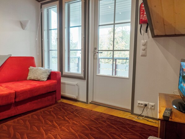 A room with a red sofa, a wooden floor, a door with a window, and a television on a wooden stand.