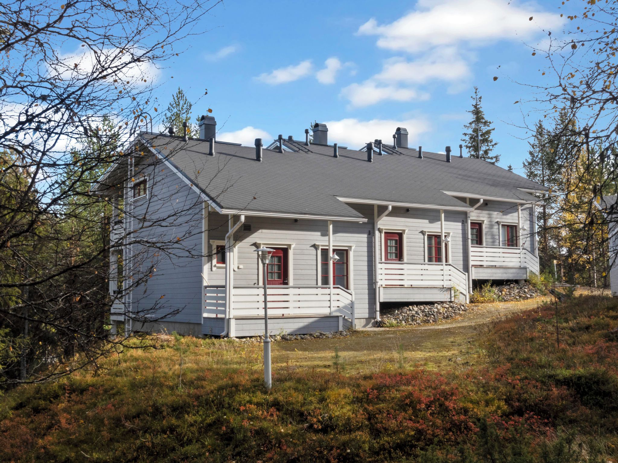 A two-story house with a grey exterior and red accents, surrounded by natural vegetation and trees.