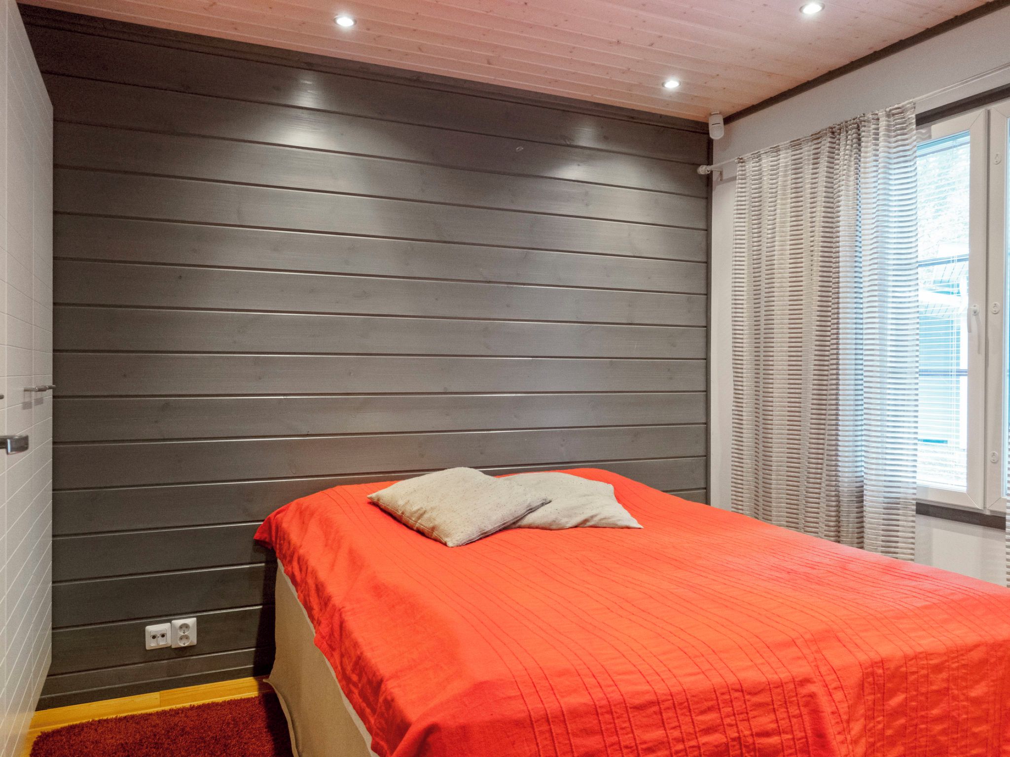Un dormitorio con cama, ventana con persianas y una pared con líneas horizontales.