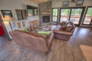 A spacious living room with a stone fireplace, leather sofas, and a wooden coffee table. - Sleepy Hollow Cabin with hot tub located in Powder House Pass (Lead)