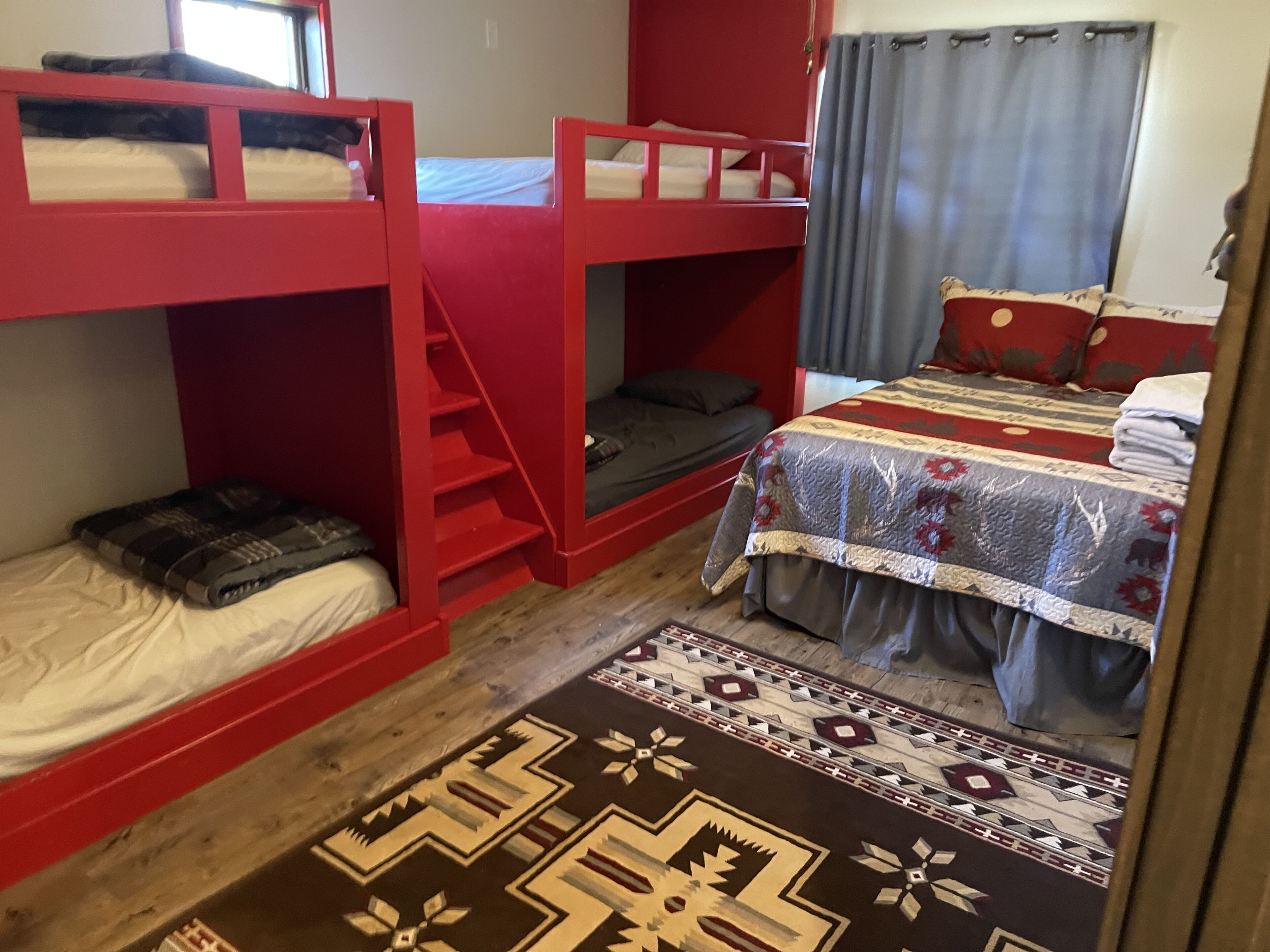A dormitory room with bunk beds, a patterned rug, and a bed with a floral bedspread.