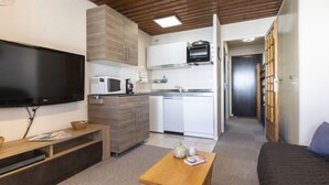 Un espace de vie compact comprenant un coin cuisine, un téléviseur à écran plat, une table basse en bois et un canapé.