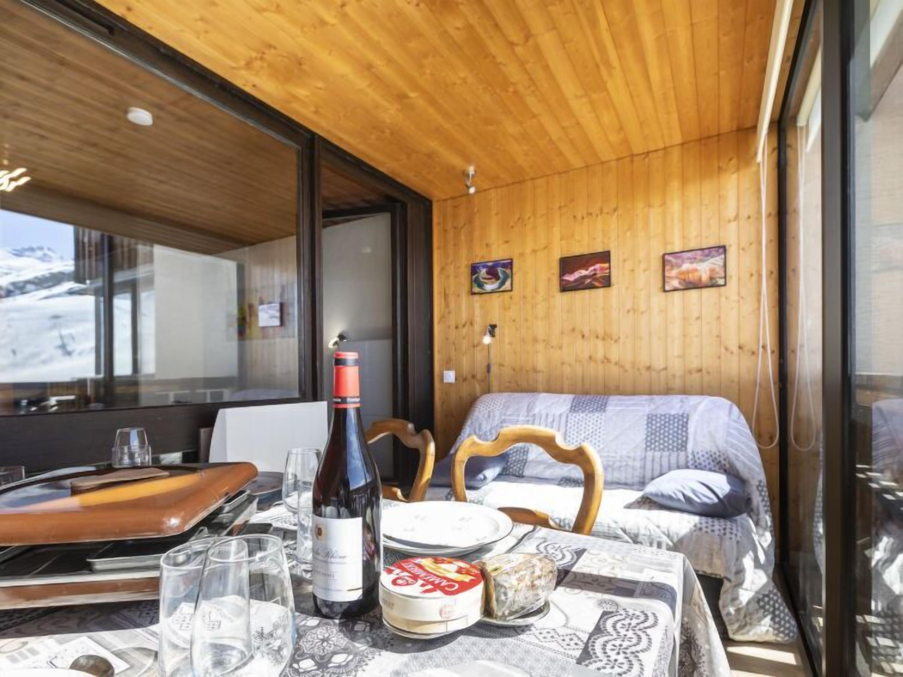 Een knus ingerichte kamer met houten plafond, een bed met een geborduurd kleed, een tafel met een fles wijn, glazen en borden.