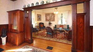 A traditional living room with a wooden floor, a red patterned rug, and a large mirror with a wooden frame. - Pinschower Inn (Cloverdale)