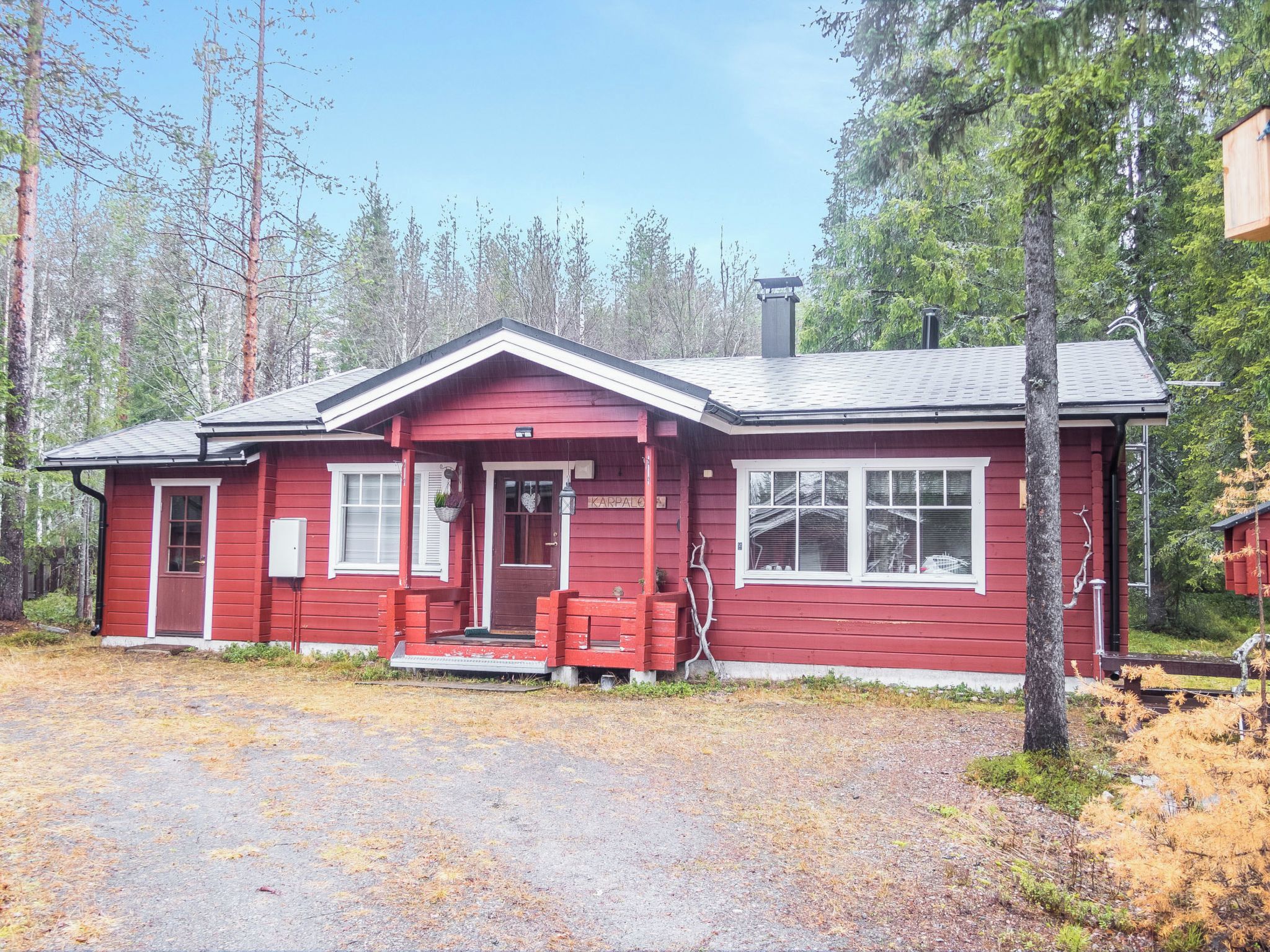 A red cabin with a front porch, a chimney, and a small porch area with a bench.