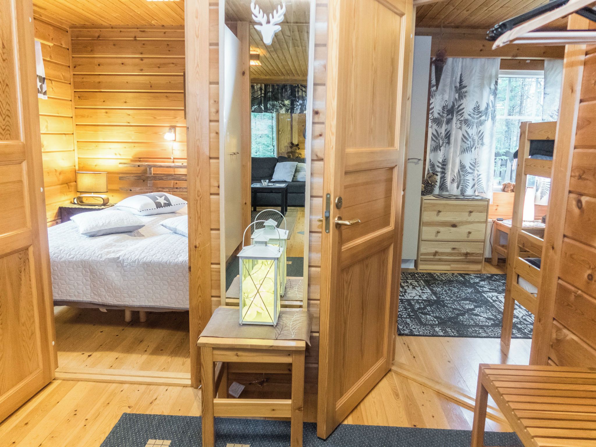 A wooden cabin interior with a bed, a small table with a lantern, a sofa, and a dresser.