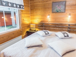 Et værelse i en træhytte med seng, puder, et natbord, en lampe og et vindue.